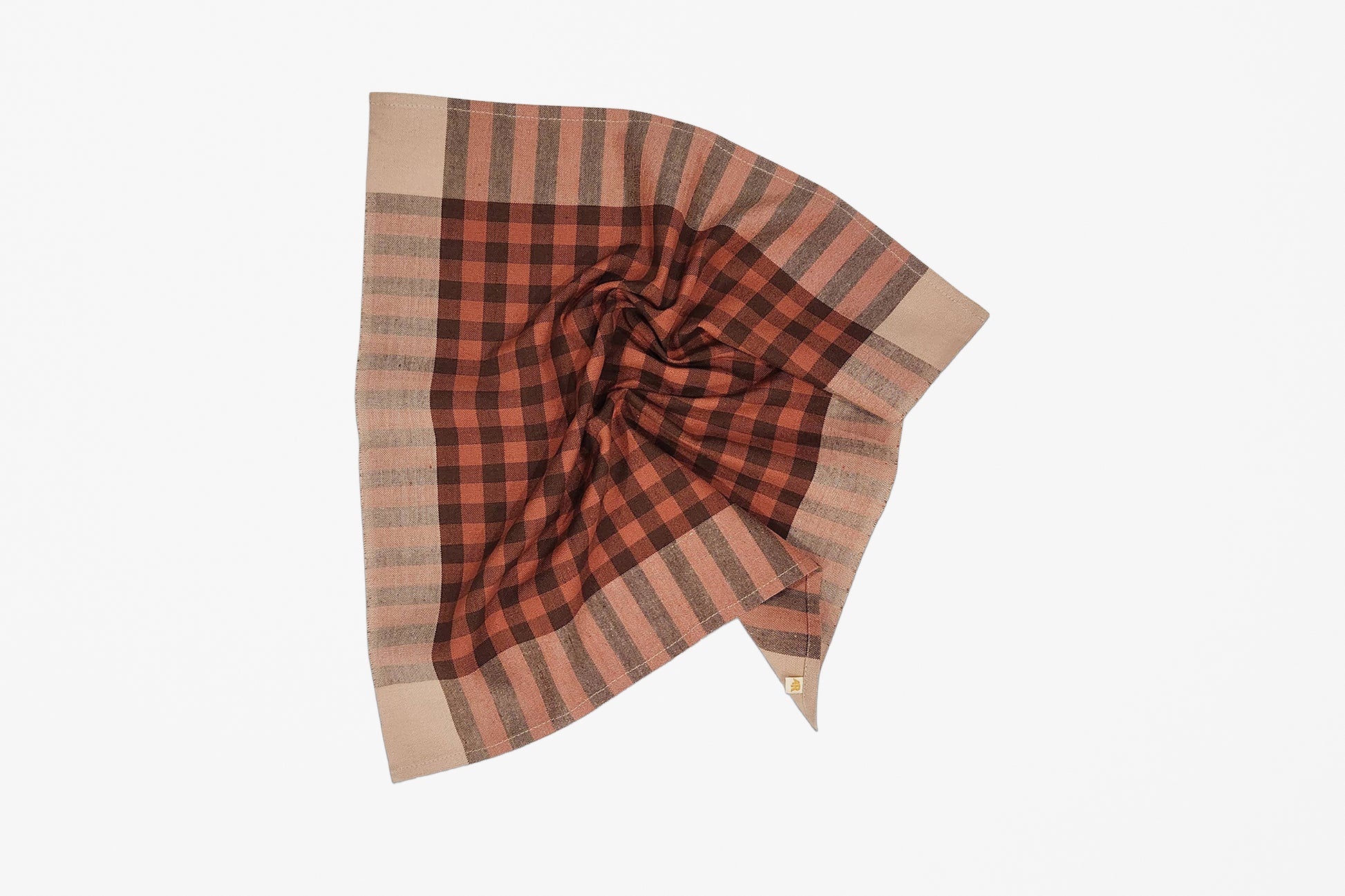 A scrunched handwoven plaid napkin in rust red, dark brown, and beige, styled in a loose swirl on a clean white background.