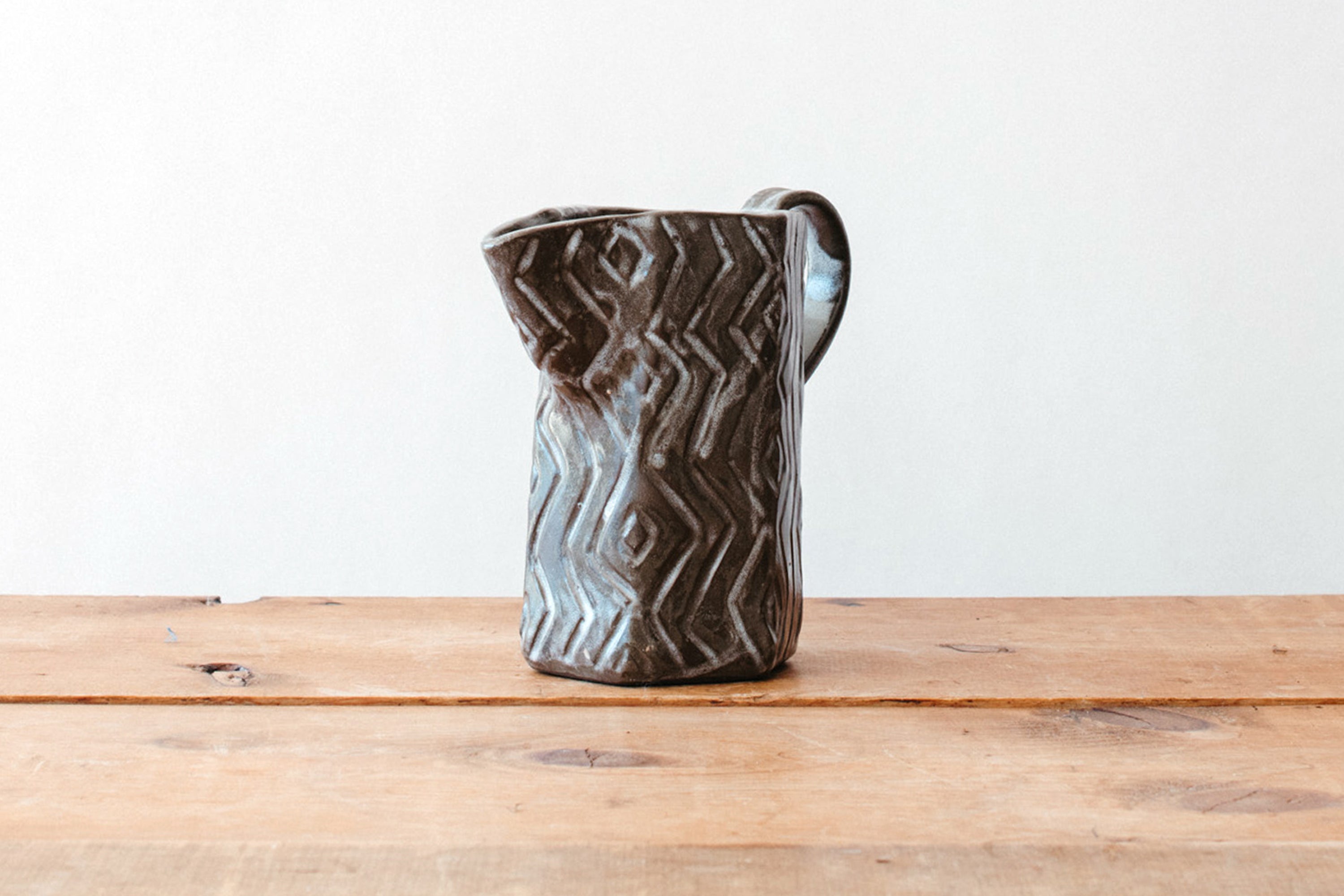 Ceramic pitcher on a wooden surface with a white background
