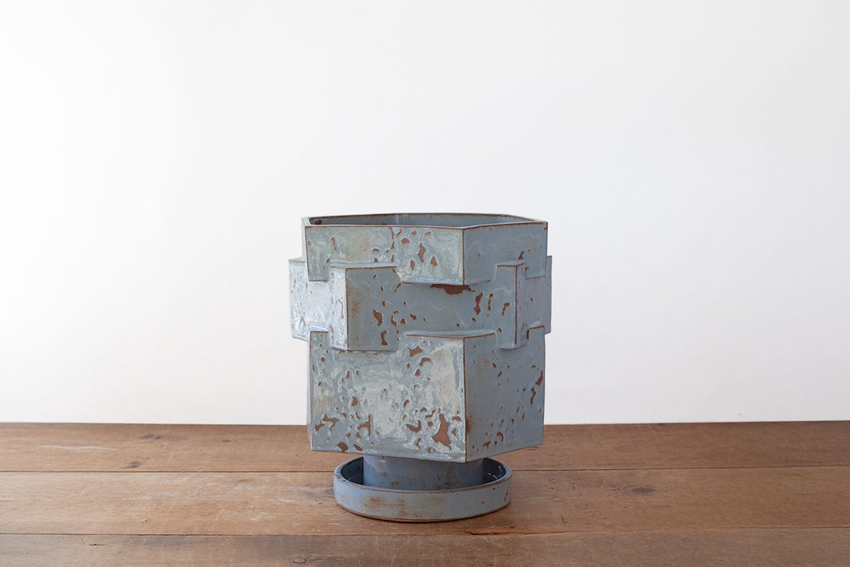 A baby blue shino-glazed hexagonal ceramic planter sitting on a wooden surface against a plain white wall.