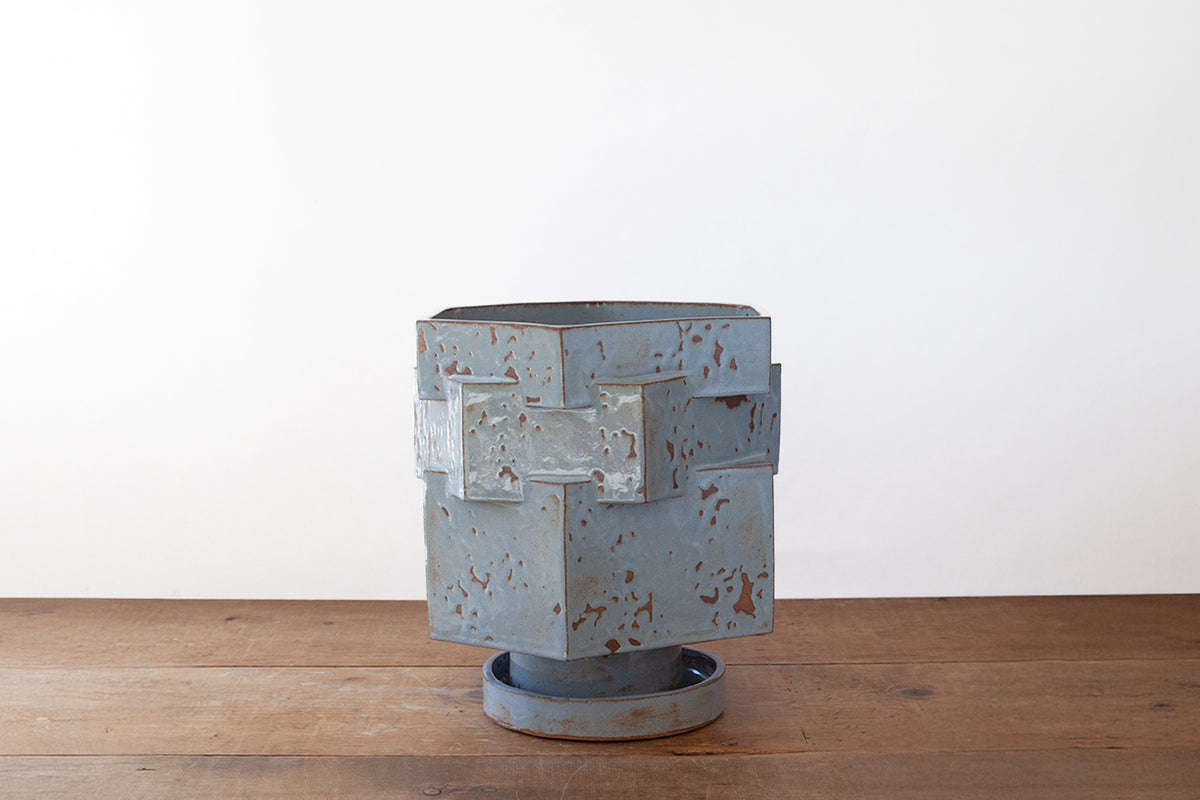 A baby blue shino-glazed hexagonal ceramic planter sitting on a wooden surface against a plain white wall.