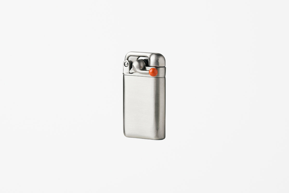 A brushed stainless steel pocket lighter with a small orange accent button, shown on a plain light gray background.