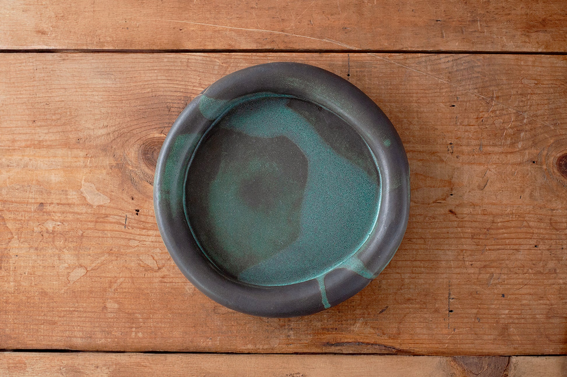 A round ceramic plate with a dark gray exterior and a teal-green glazed interior on a rustic wooden surface.