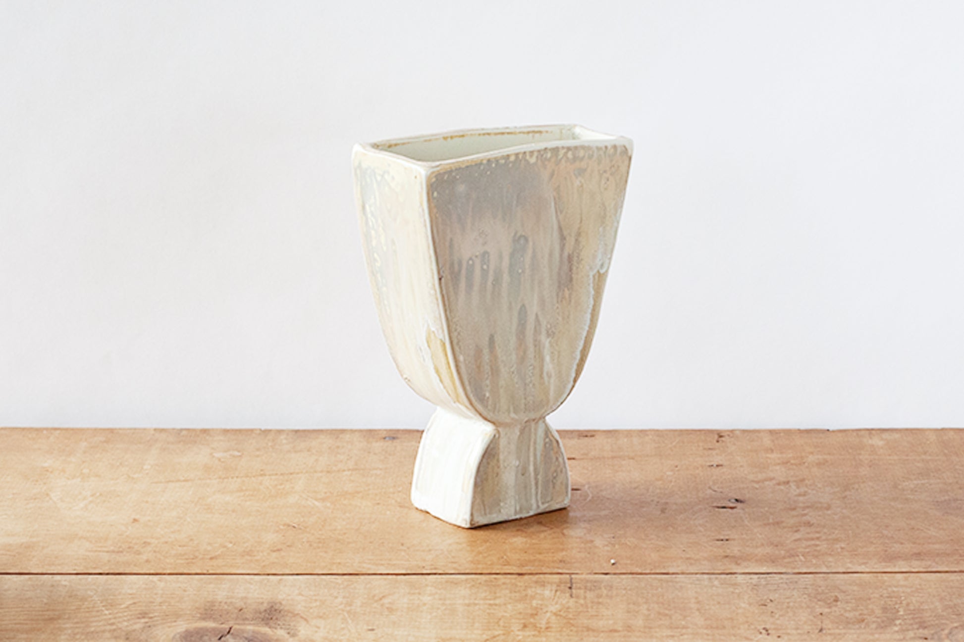 A ceramic planter with a textured, glazed finish in cream and light brown tones, sitting on a rustic wooden surface against a plain white wall.