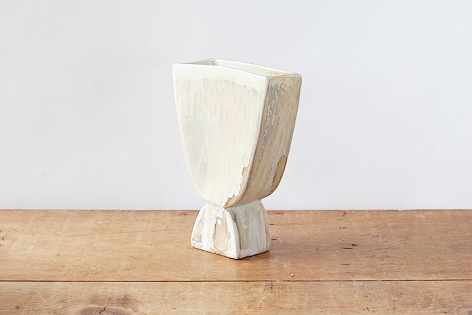 A small sculptural ceramic planter with a wide, open top and a pedestal base, shown on a rustic wooden tabletop against a plain white wall.