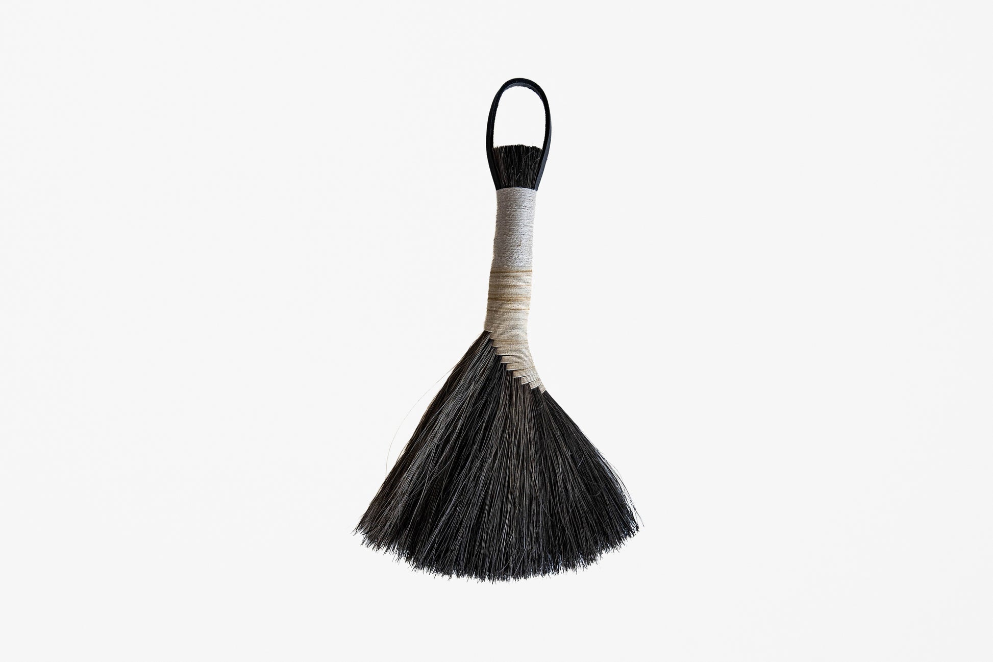 A traditional hand broom with black bristles, a beige wrapped handle, and a black hanging loop, shown against a plain white background.