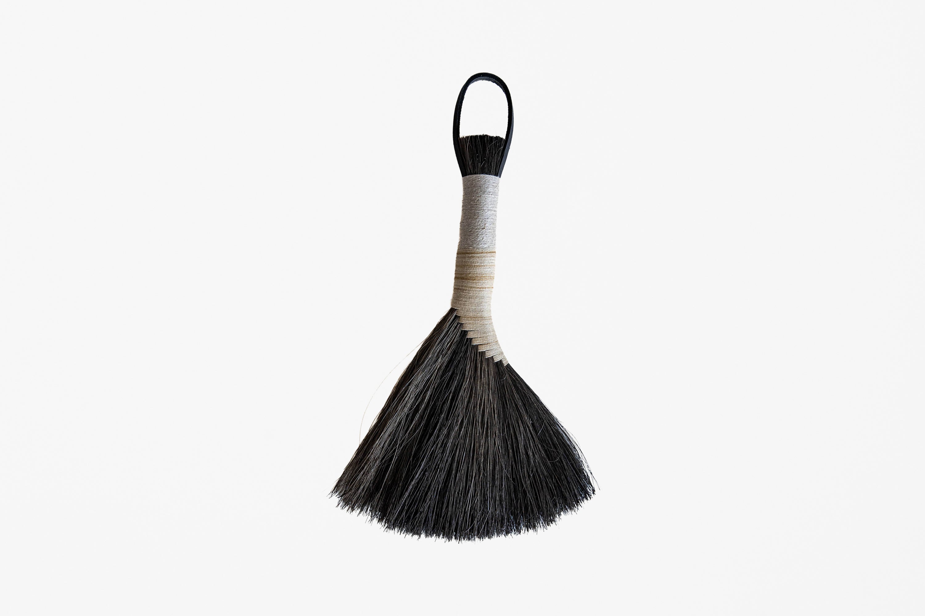 A traditional hand broom with black bristles, a beige wrapped handle, and a black hanging loop, shown against a plain white background.