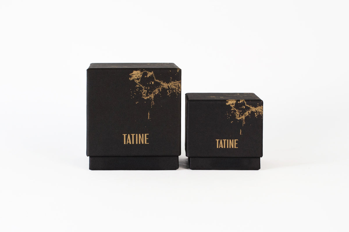 Two black candle boxes made from recycled paper with gold text and design on a white background